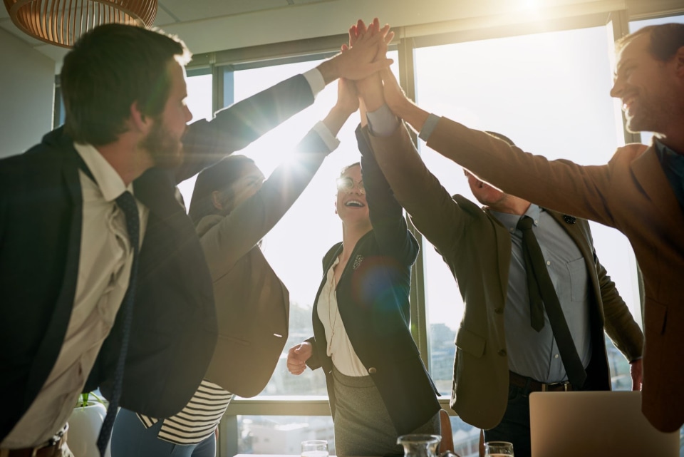 A team celebrating success with high-fives in a bright office, sunlight streaming through large windows, creating a cheerful atmosphere.